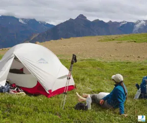 Female backpacker sitting beside tent and backpack with mountains in background